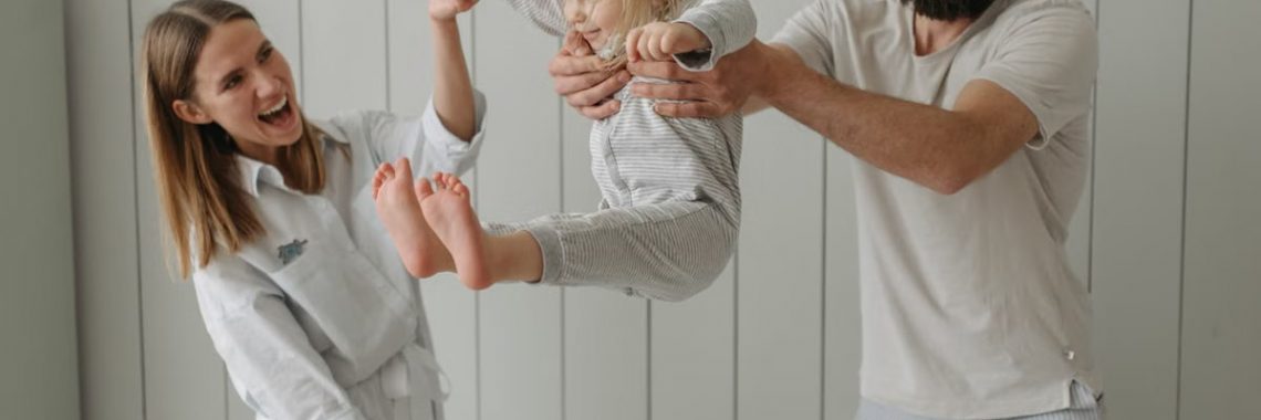 Joyful parents playing with their daughter indoors, all wearing white, capturing a moment of happiness.